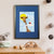 A young white boy with blonde hair sits on a cloud that brings him up to a giraffe's face (A3 framed with blue mount)