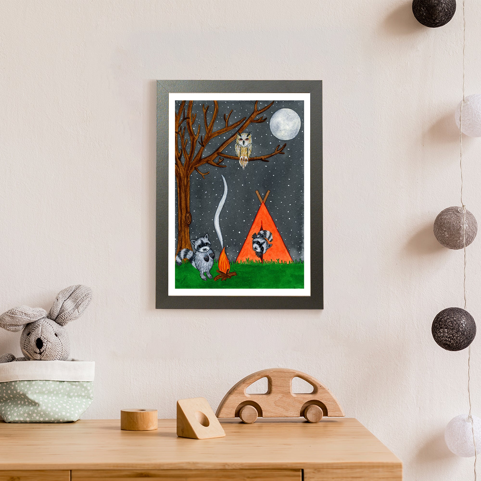 Against a starry night, a racoon warms his hands by a log fire as another watches from inside an orange tent, while a brown owl watches on (print only)