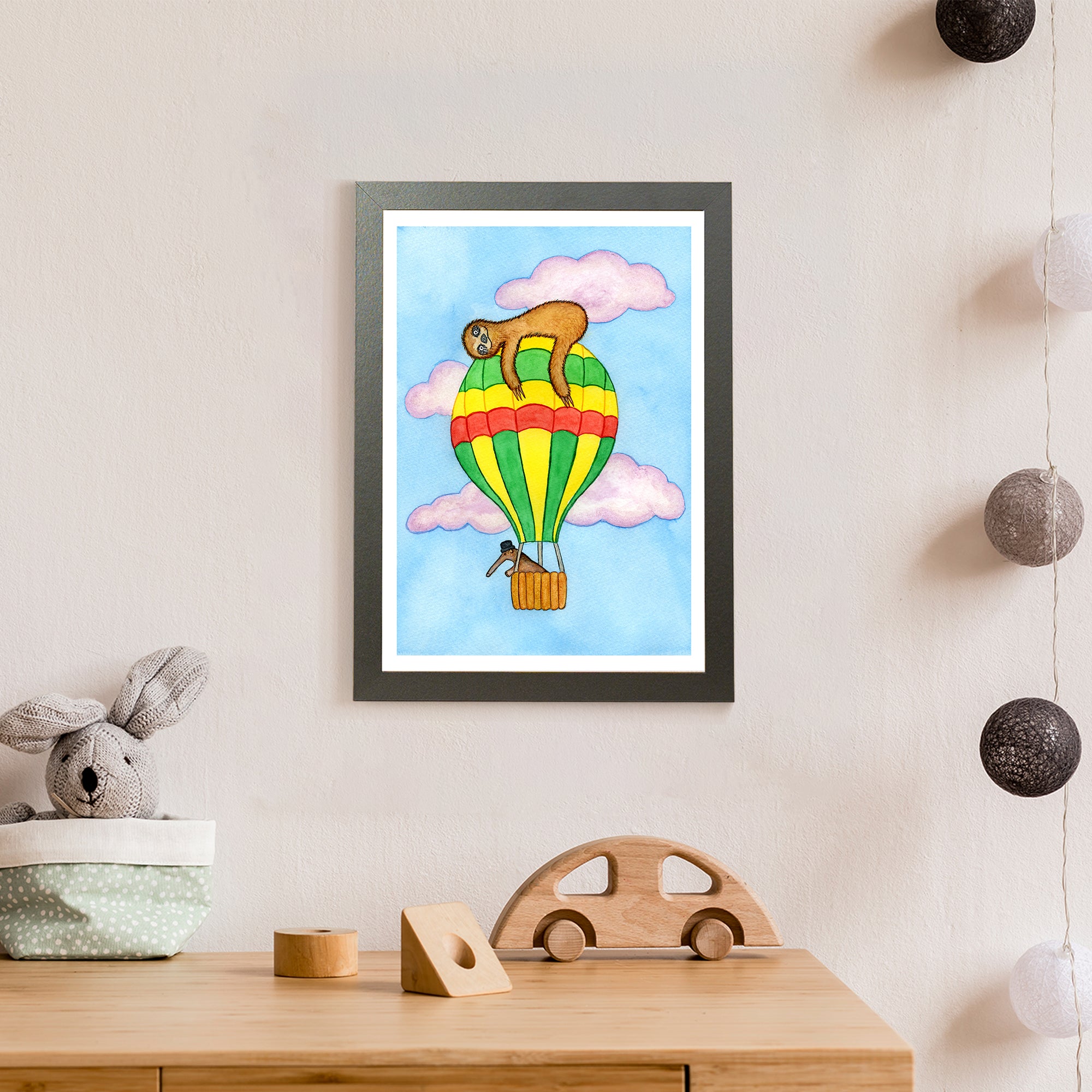 A sleepy brown sloth lies on top of a green, red, and yellow hot air balloon being steered into the clouds by an anteater wearing a hat (print only)