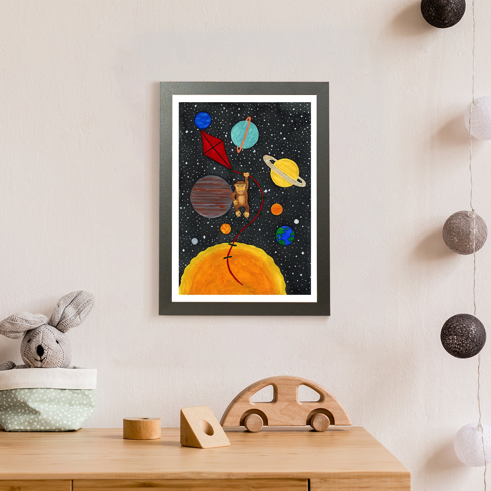 A brown monkey holds on to a red kite among the sun, stars and planets in space (print only)
