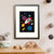 A grey bunny looks out of the window of a red, white and blue rocket, as it flies through space amongst colourful planets, stars and comets (A3 framed with white mount)